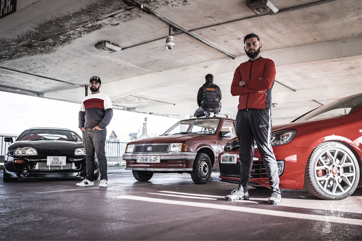 Three men standing next to cars