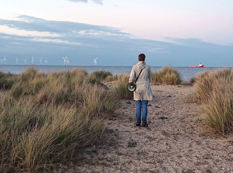 Back of a woman carrying a megaphone, looking out to sea