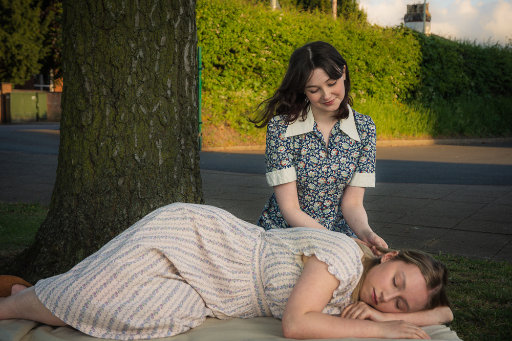 A girl strokes the hair of another girl who is lying down in front of her