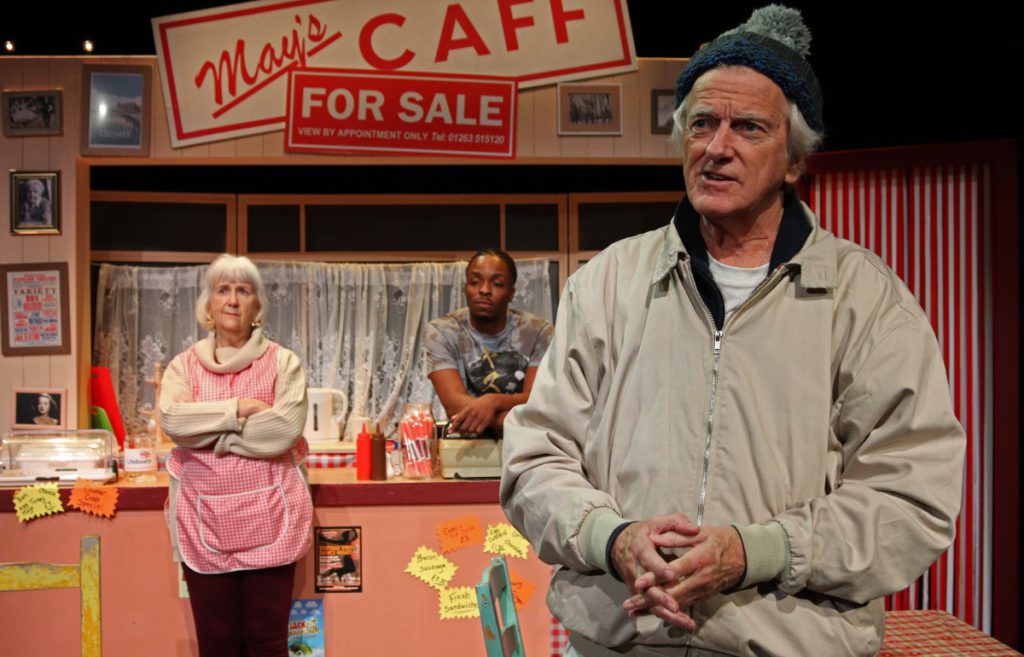 Three people stand in a cafe set for the play Time and Tide